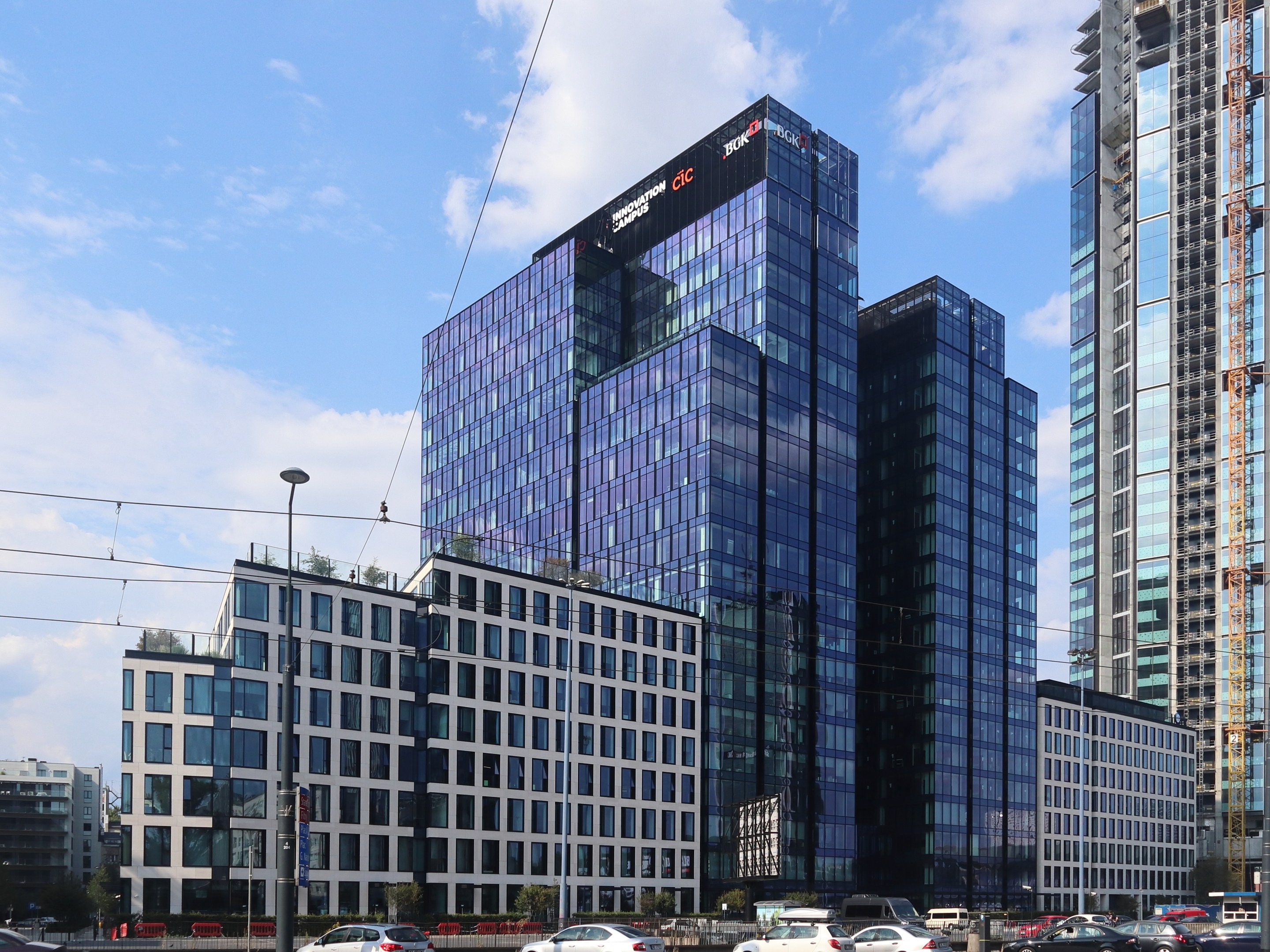 Außenansicht des Deutschen Bank-Hauptsitzgebäudes in Frankfurt, Deutschland, mit umgebender städtischer Infrastruktur einschließlich Straßenlaternen, Fahrzeugen und Bäumen.
