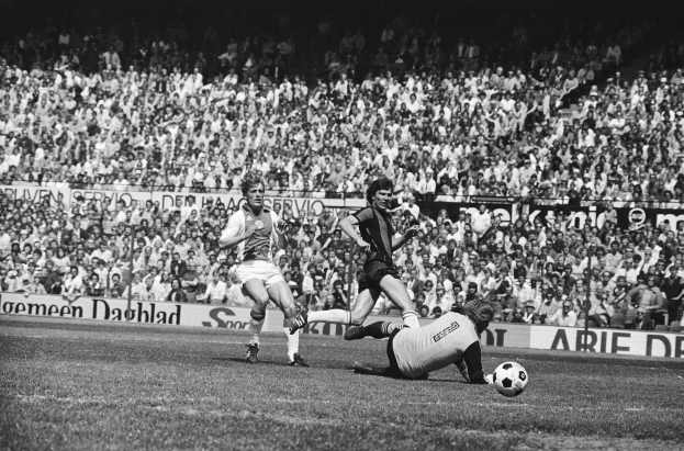 Schwarzes Foto von Männern, die auf einem Feld Fussball spielen, mit Zuschauern im Hintergrund und einer Fahne mit der Aufschrift "Bundesliga 1978-79 Ajax 1-1 Hannover 96."