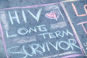 Ein hellgrauer Gehweg mit den Worten "HIV Love Long Term Survivor" in fetter, schwarzer Kreide geschrieben.