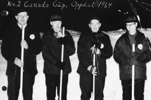 Vier Männer in Jacken und Mützen stehen im Schnee und halten Hockey-Schläger, mit dunklem Hintergrund und Text oben.