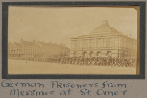 Eine Gruppe deutscher Gefangener aus Messines steht vor einem Gebäude unter einem klaren blauen Himmel, mit Text am unteren Bildrand.