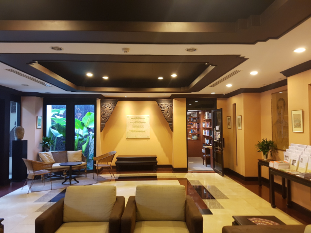 Ein hell erleuchteter Hotelfoyer mit Sitzbereichen mit Sofas und Stühlen, Tischen, Zimmerpflanzen, Bücherregalen, Wandbehängen und dekorativen Seitentischen, entworfen zum Entspannen.