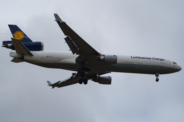 Ein Lufthansa Cargo Boeing 777-300ER im Flug, mit ausgefahrenen Flügeln und laufenden Triebwerken, mit sichtbarem Text auf der Rumpfseite gegen einen bewölkten Himmel.