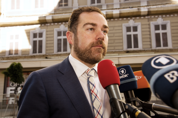 Ein Mann im Anzug und Krawatte steht vor Mikrofonen und spricht zu den Medien vor einem Gebäude, nachdem er zu drei Jahren Haft verurteilt wurde.