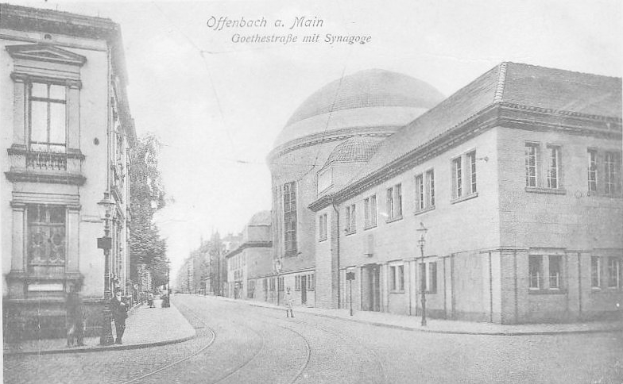 Ein altes Schwarz-Weiß-Foto einer Stadtstraße namens Goethestraße in Offenbach am Main, das Gebäude, Straßenlaternen, Bäume und Menschen zeigt, die auf der Straße gehen, mit der Aufschrift "Offenbach a Main, Goethestraße mit Synagoge" oben.