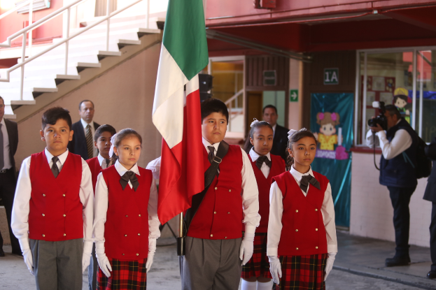 Eine Gruppe von Schülern in Schuluniformen steht zusammen, einer hält eine Fahne, mit Menschen, einer Kamera, einem Gebäude, einem Schild, einer Fahne und einer Treppe im Hintergrund.