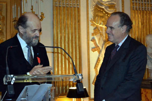 Ein Podium mit Mäusen oben drauf, ein Mann auf der rechten Seite, der lächelt, eine Statue, ein Kerzenständer und eine Wand mit Entwürfen im Hintergrund.