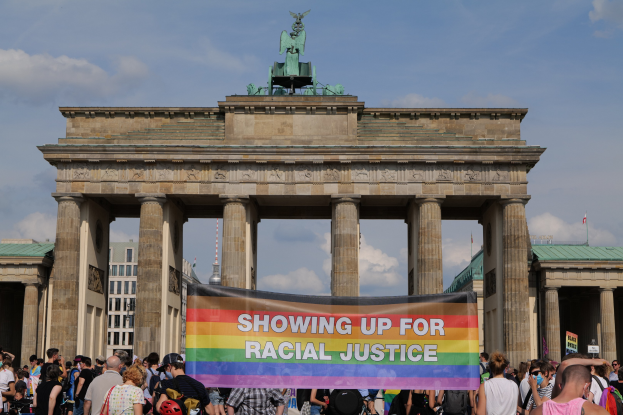 Eine Gruppe von Menschen, die vor dem Brandenburger Tor in Berlin, Deutschland, mit einem Banner stehen, auf dem die Wörter "Rassische Gerechtigkeit" geschrieben sind.