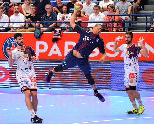Männer beim Handballspielen auf einem Feld mit einem Ball in der Mitte, Zuschauern im Hintergrund und einer Tafel mit der Aufschrift "Futsal-Weltmeisterschaft 2015 - Paris Saint-Germain vs. Olympique Lyon".