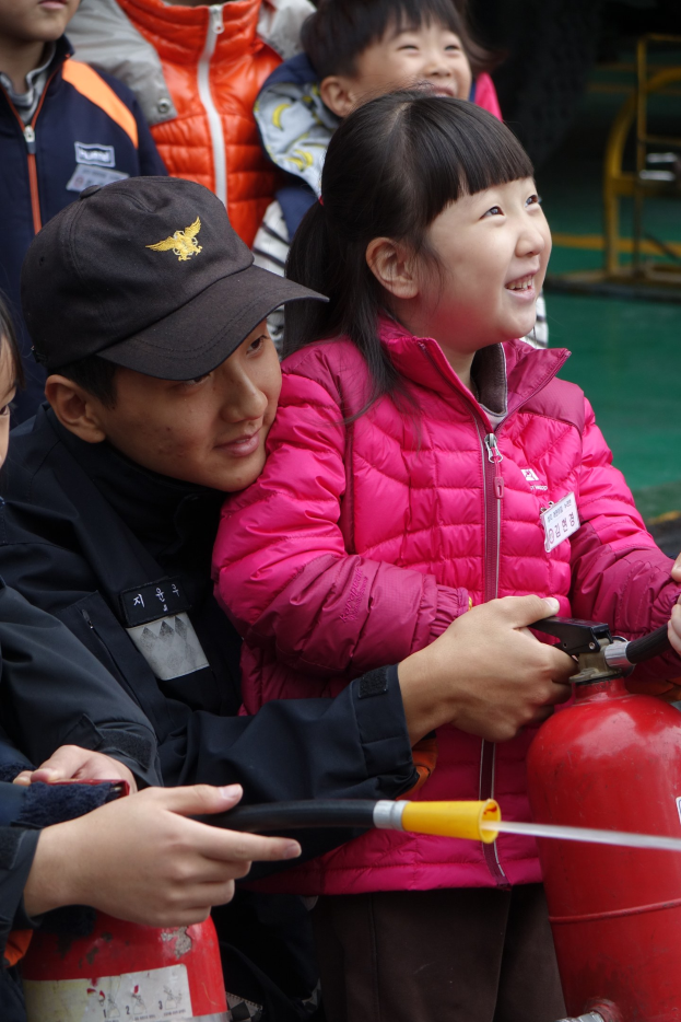 Eine Gruppe von Kindern umringt einen roten Hydranten in einer Schulumgebung, wobei eines der Kinder eine Leitung hält.