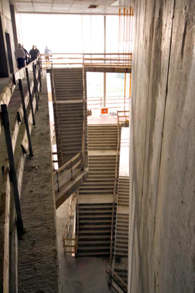 Eine Treppe mit einer Decke oben, einer großen Wand auf der rechten Seite, einem hölzernen Zaun auf der linken Seite und einigen Menschen mit Helmen auf den Stufen.