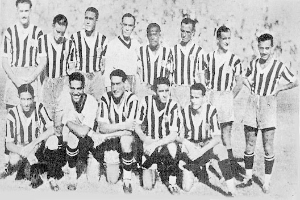 Ein Schwarz-Weiß-Foto einer Fußballmannschaft, wobei einige Spieler stehen und andere auf dem Boden sitzen, und ein Text unten.