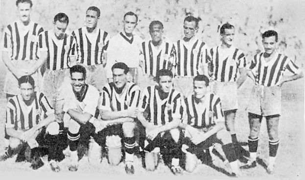Ein Schwarz-Weiß-Foto einer Fußballmannschaft, wobei einige Spieler stehen und andere auf dem Boden sitzen, und ein Text unten.