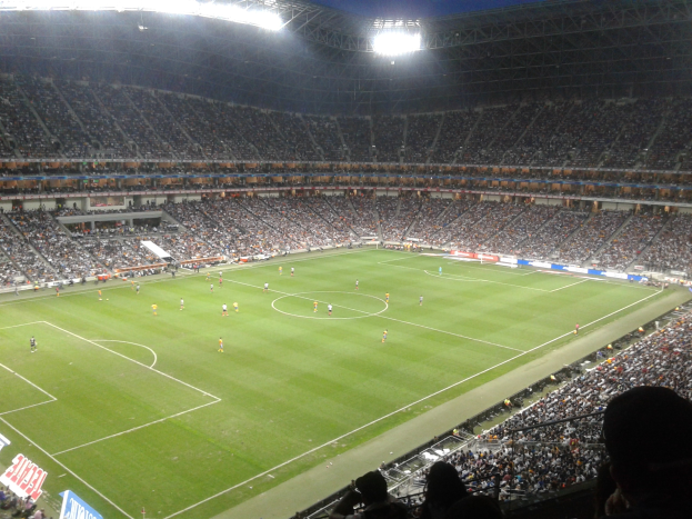 Ein hell erleuchtetes Fußballstadion voller jubelnder Zuschauer, die ein Spiel verfolgen, umgeben von Werbetafeln.
