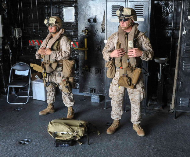 Zwei Soldaten mit einer Tasche vor sich, ein Stuhl und andere Gegenstände im Hintergrund.
