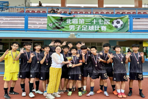 Gruppe junger Männer in Fußballtrikots auf einem Feld, die Medaillen tragen und einen Pokal halten, mit einem 'Yokohama U-16 Jungen Fußballteam' Banner im Hintergrund und sitzenden Zuschauern.